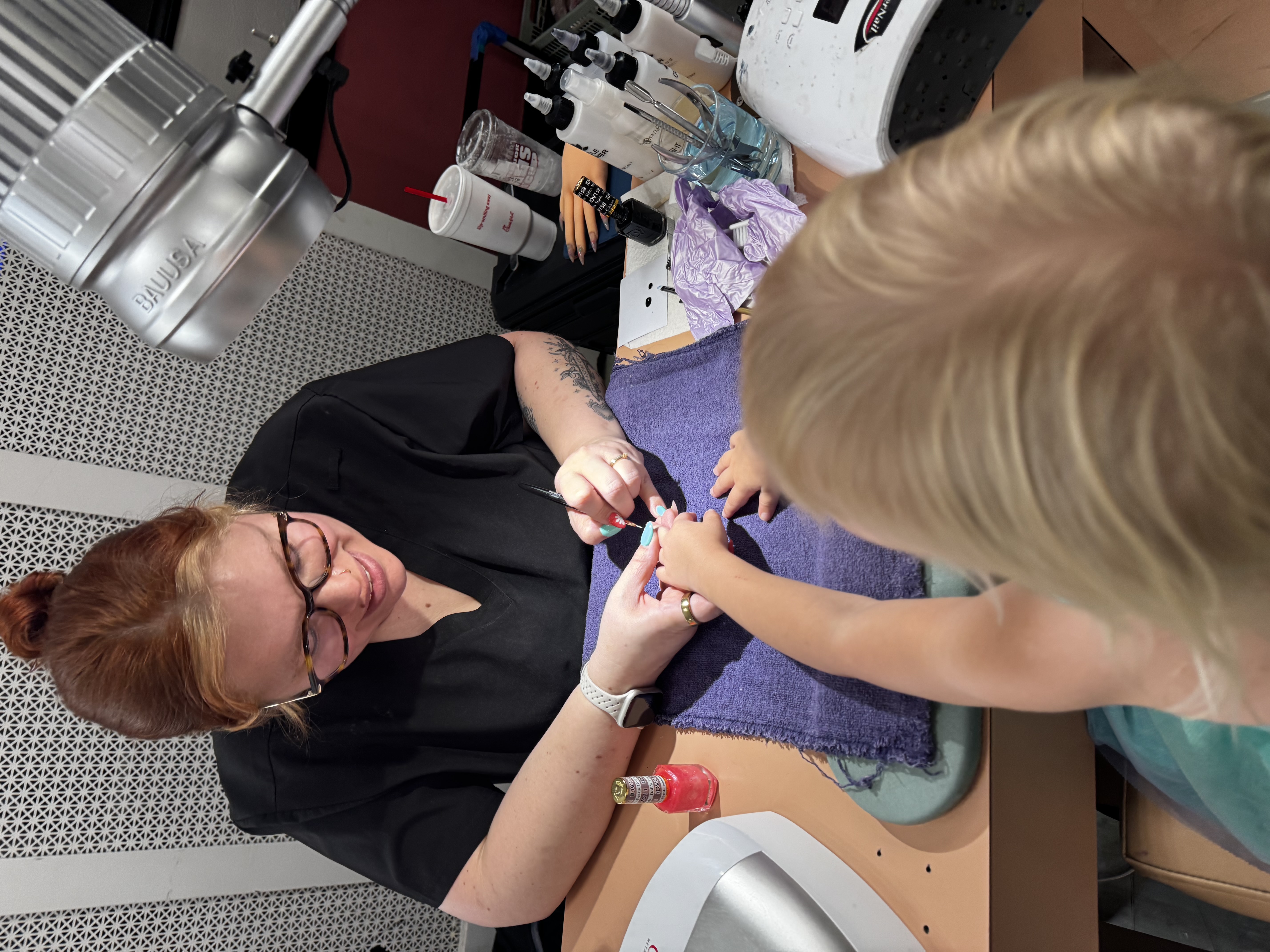 Jacklyn painting a young client’s nails